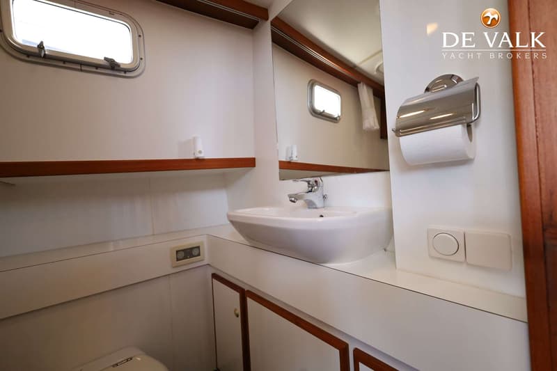 Een badkamer met een wastafel, spiegel, toiletrolhouder, een raam en houten accenten.