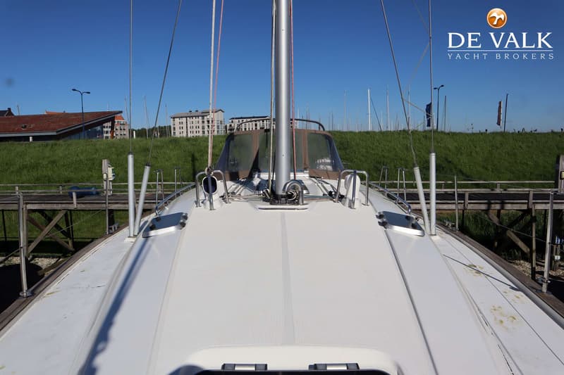 Een bovenaanzicht van het voordek van een zeilboot met een mast, lijnen, relingen en een bruine buiskap, liggend aan een…