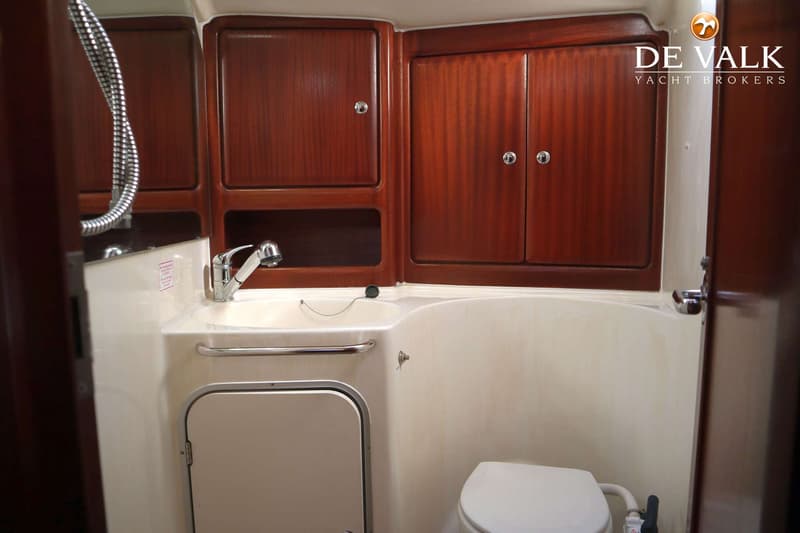 Een badkamer met een wastafel, kraan, douchekop, toilet en houten kasten.