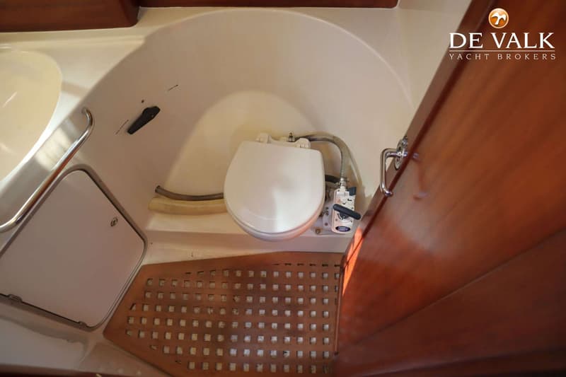 Een boottoilet met een houten rooster op de vloer en een houten deur aan de rechterkant.