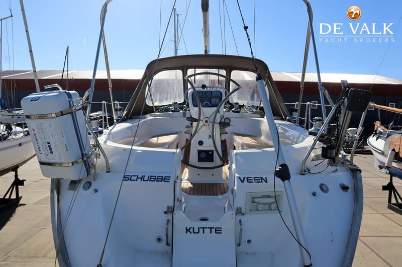 Een witte zeilboot met een bruine buiskap en een stuurwiel in de kuip, met de namen "SCHUBBE", "VEEN" en "KUTTE" op de…
