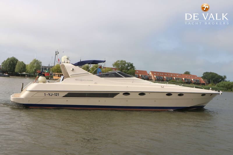 Een beige motorjacht met blauwe strepen en de registratie "1-YJ-121" vaart op het water.