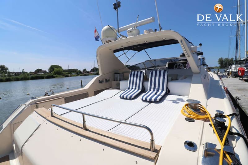 Een boot ligt aan een kade met twee gestreepte stoelen en een Nederlands vlaggetje aan de achterzijde. — Riva 60 Bahamas