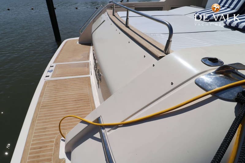 Een deel van een boot met teakhouten dek, een reling en een geel touw, liggend aan het water. — Riva 60 Bahamas