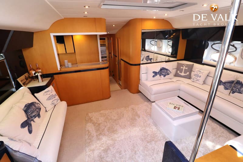 Een interieur van een boot met een witte bank, kussens met vissen en ankers, een salontafel en een bar. — Riva 60 Bahamas