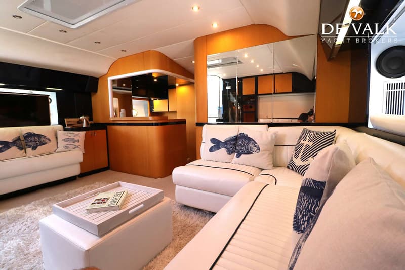 Een interieur van een boot met witte banken, kussens met vismotieven, een salontafel en houten kasten. — Riva 60 Bahamas