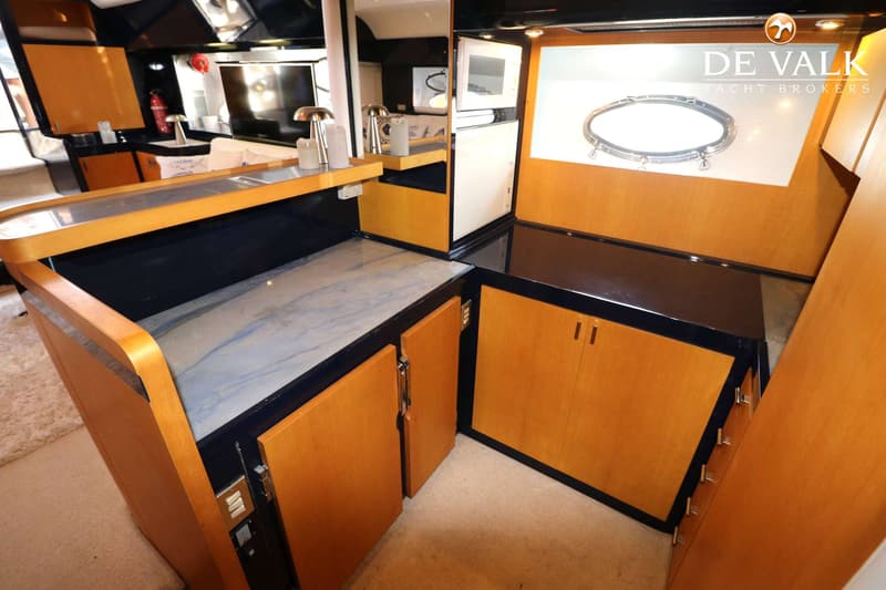 De foto toont een interieur van een boot met houten kasten, een marmeren aanrecht en een patrijspoort. — Riva 60 Bahamas