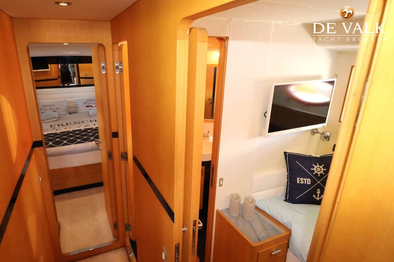 Een gang met houten panelen leidt naar een slaapkamer met een bed en een televisie aan de muur.