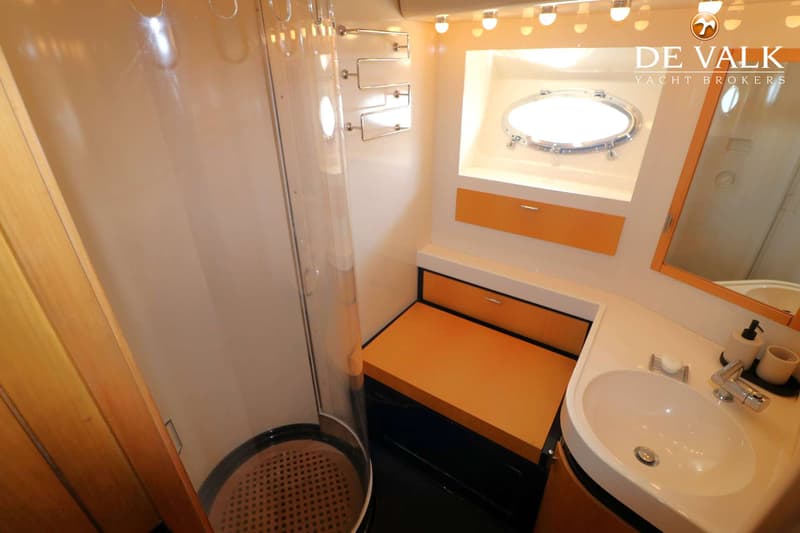 Een badkamerinterieur met een douchecabine, een wastafel met spiegel en een patrijspoort.