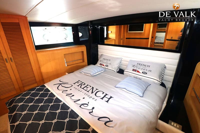 Een kajuit met een tweepersoonsbed, kussens en dekbed met de tekst "FRENCH Riviera saint-tropez", en een spiegel.