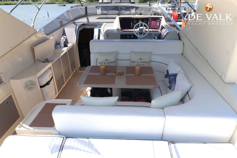 Een bovenaanzicht van het dek van een boot met witte banken, een houten tafel en een stuurconsole. — Riva 60 Bahamas