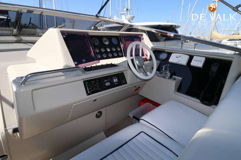 De foto toont de stuurstand van een boot met een wit stuurwiel, diverse meters en schakelaars, en witte bekleding.