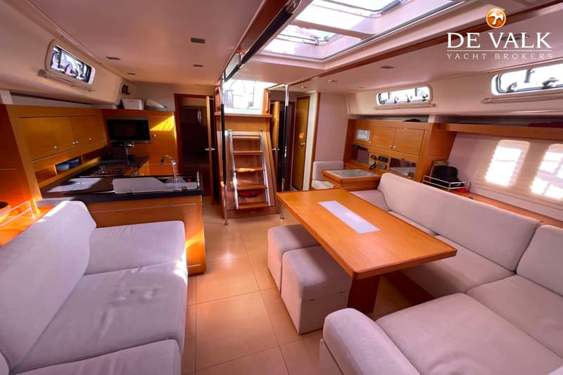 De foto toont het interieur van een boot met een kombuis, zithoek met tafel en een trap naar een hoger dek. — Hanse 545