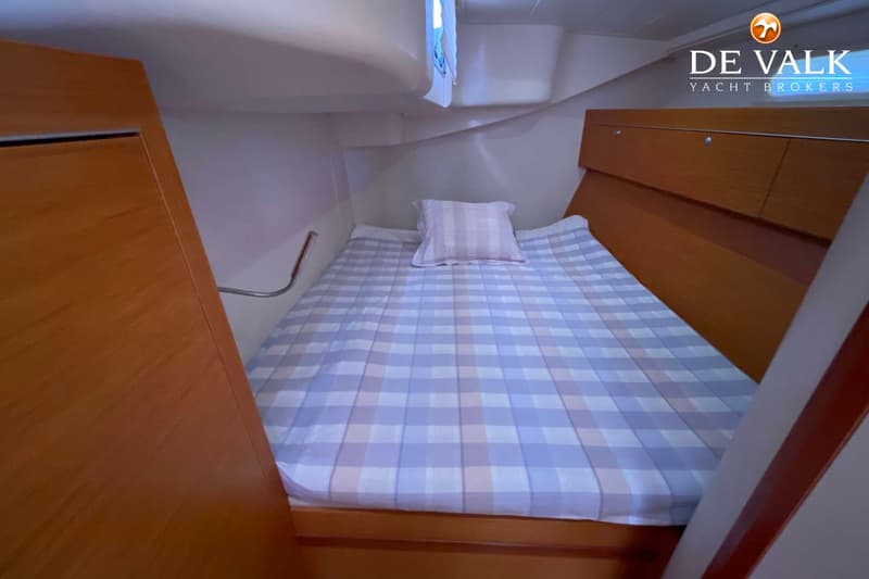 Een kajuit met een bed met een geruit dekbed en kussen, omringd door houten en witte panelen. — Hanse 545