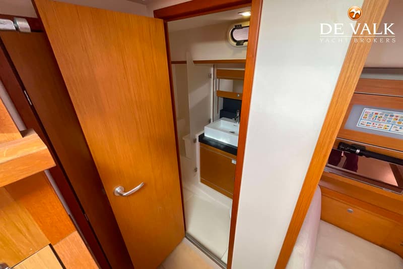 Een openstaande houten deur toont een badkamer met een witte wastafel en een spiegel.