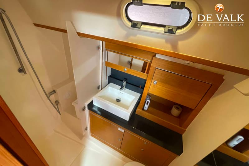 Een badkamer aan boord met een douche, wastafel, spiegel, houten kasten en een patrijspoort.