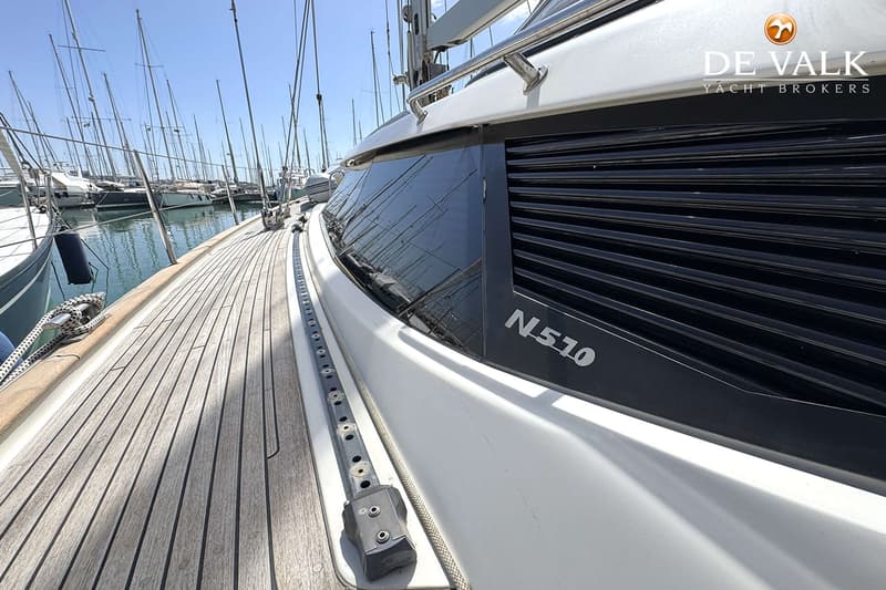 Een dek van een boot met houten planken, een raam met "N 510" erop en een logo van "DE VALK YACHT BROKERS". — Najad 570
