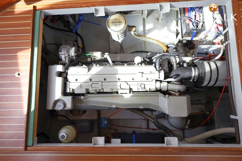 Een close-up van een scheepsmotor met diverse slangen, kabels en filters, omringd door houten en grijze panelen.