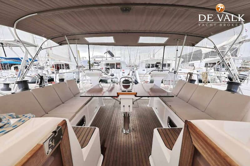 De foto toont de kuip van een zeilboot met een houten vloer, een tafel en zitbanken met kussens onder een bimini.