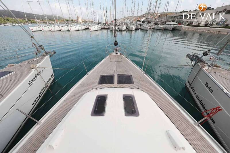 Een bovenaanzicht van het voordek van een zeilboot met twee luiken, omringd door teakhouten dekken, in een haven vol andere…
