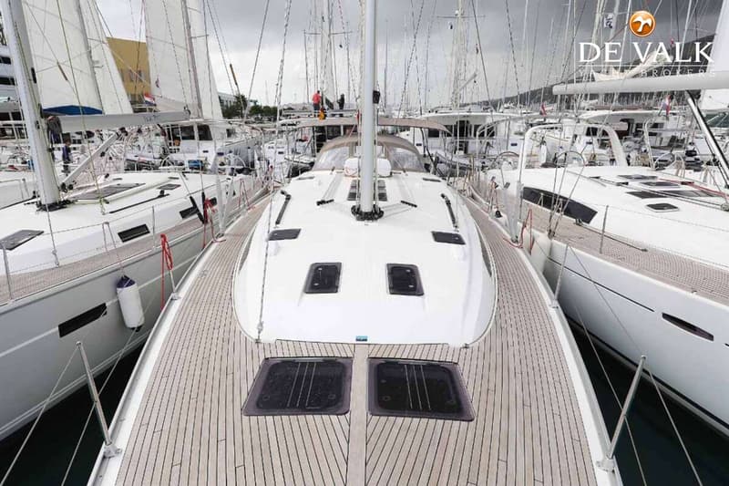 Een bovenaanzicht van het dek van een zeilboot met een houten dek en twee grote luiken, omringd door andere boten.