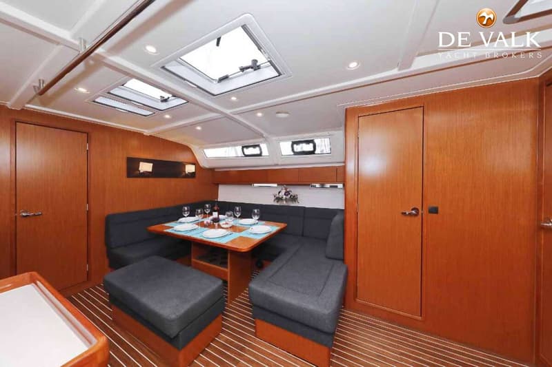 De foto toont een interieur van een boot met een houten vloer, een eettafel met servies, en grijze zitbanken.