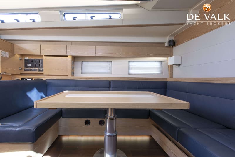Een interieur van een boot met een houten tafel, donkerblauwe banken en houten kasten. — Hanse 588