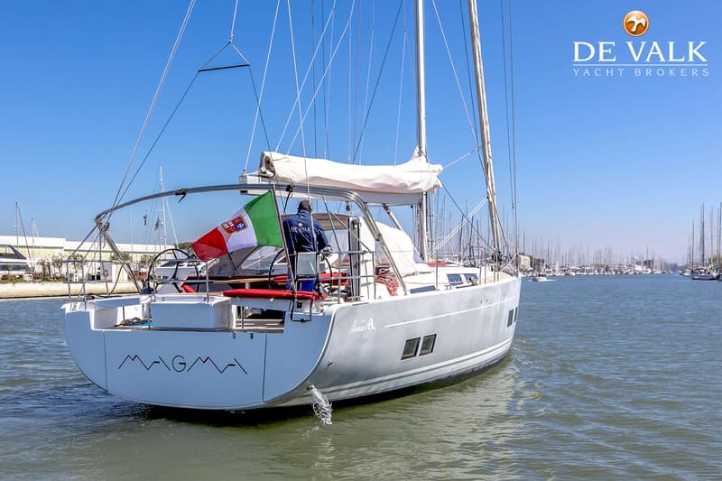Een zeilboot met de naam "MAGMA" vaart op een zonnige dag door een jachthaven, met een Italiaanse vlag aan de achtersteven.