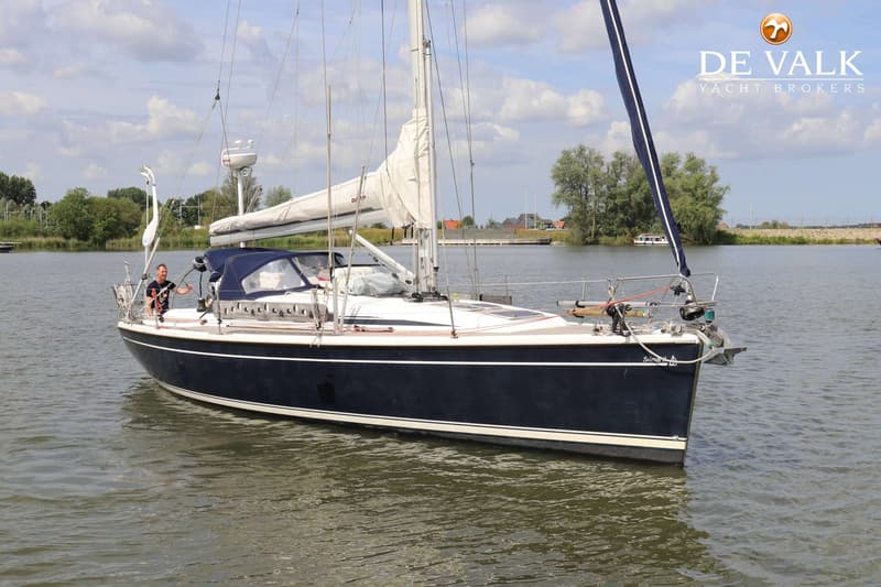 Een donkerblauwe zeilboot met witte strepen en een witte opbouw vaart op een waterweg. — Dehler 39 SQ
