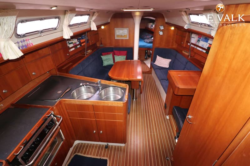 De foto toont het interieur van een boot met een kombuis, zithoek, tafel en een bed in de boeg. — Dehler 39 SQ