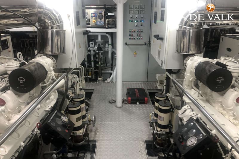 Een machinekamer met twee witte MAN-motoren, een grijs bedieningspaneel en een geruite vloer.