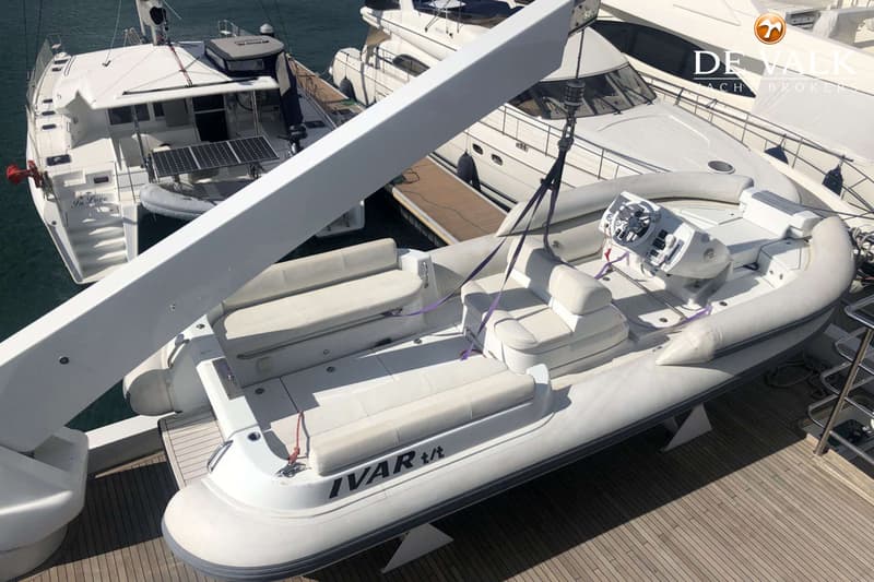 Een witte rubberboot met de naam "IVAR t/t" hangt aan een kraan boven een houten dek.