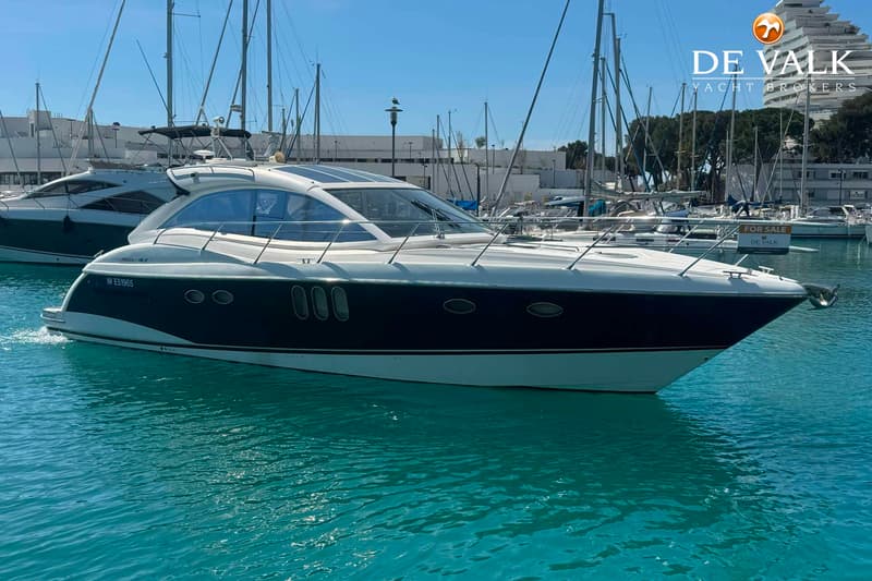 Een donkerblauwe en witte motorboot ligt in een jachthaven met andere boten en gebouwen op de achtergrond. — Absolute 47 HT