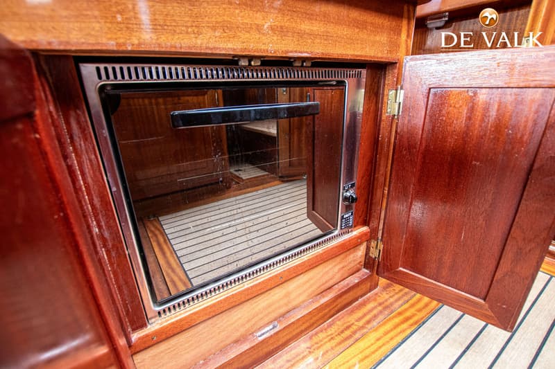 Een ingebouwde oven met een glazen deur en een zwarte handgreep, omringd door houten kasten en een houten vloer.