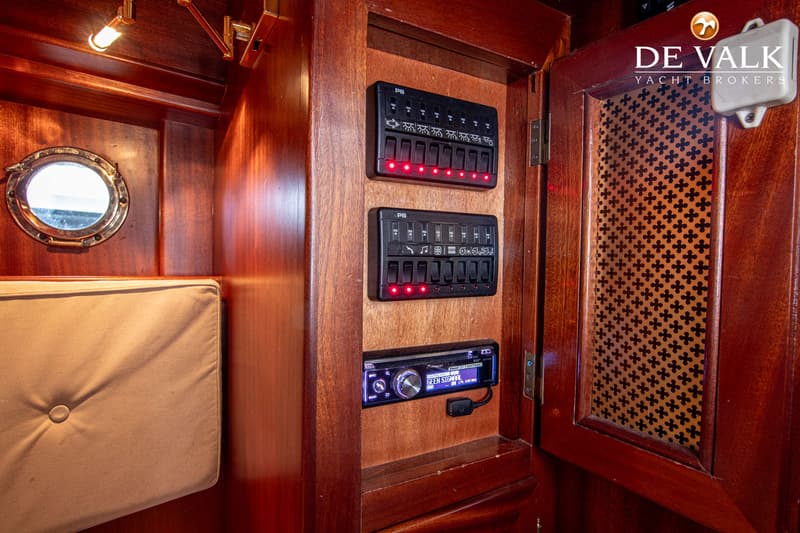 Een interieur van een boot met houten wanden, een patrijspoort, een kussen, schakelpanelen en een radio. — Breedendam MTB 31