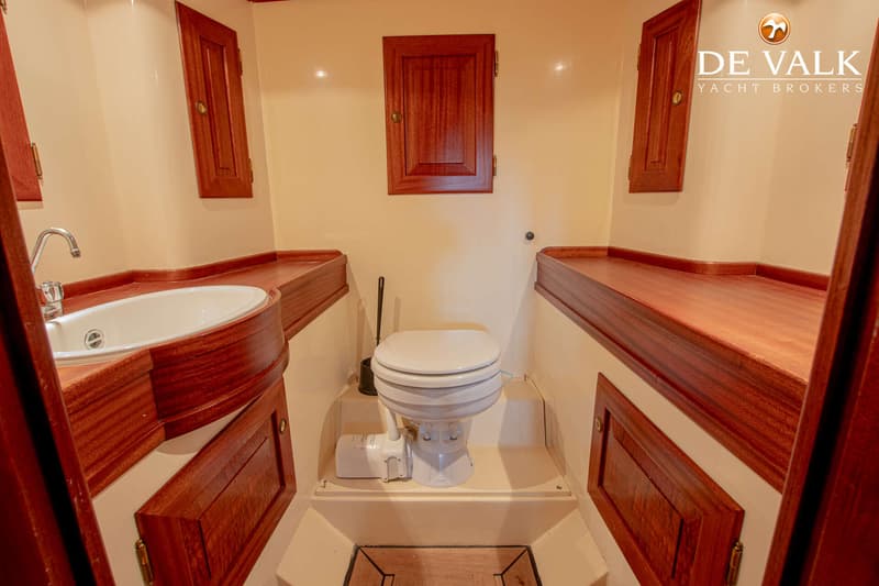 Een toiletruimte met een wit toilet, een wastafel met kraan en houten kasten en afwerkingen.