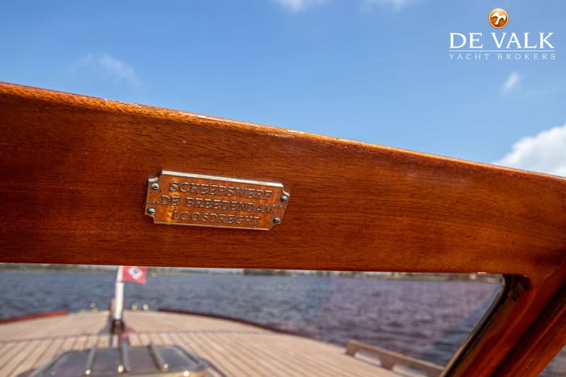 Een detailfoto van een houten boot met een metalen plaatje met de tekst "SCHEEPSWERF DE BREEDENDAM LOOSDRECHT".
