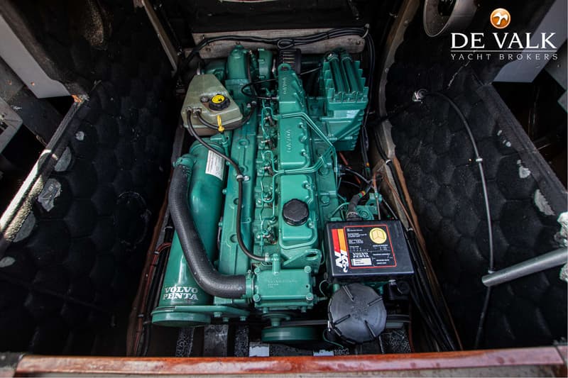 Een groene Volvo Penta motor met een zwarte accu en diverse slangen en kabels is zichtbaar in een motorruimte.