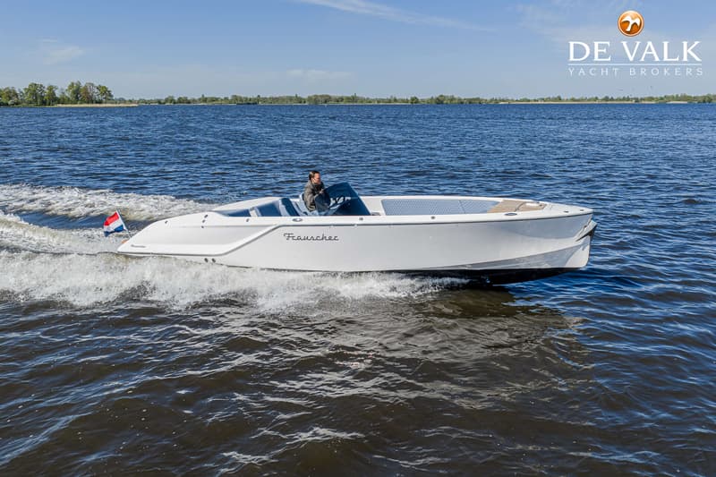 Een witte motorboot met een man aan het roer vaart op blauw water, met een Nederlandse vlag aan de achtersteven.