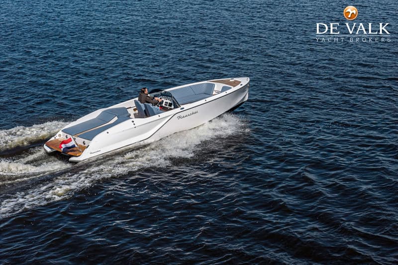 Een witte motorboot met een man aan het roer vaart over donkerblauw water, met een Nederlandse vlag achterop.