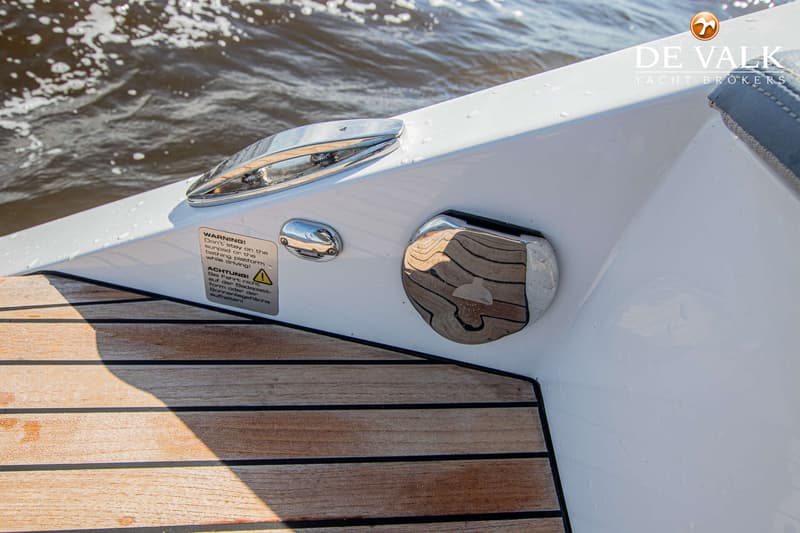 Een detailfoto van de achtersteven van een boot met een houten dek en een waarschuwingssticker. — Frauscher 858 Fantom Air