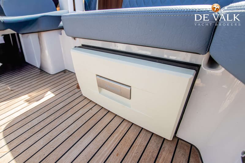 Een witte Dometic koelkast is zichtbaar onder een blauwe bank, met een houten dek op de voorgrond.