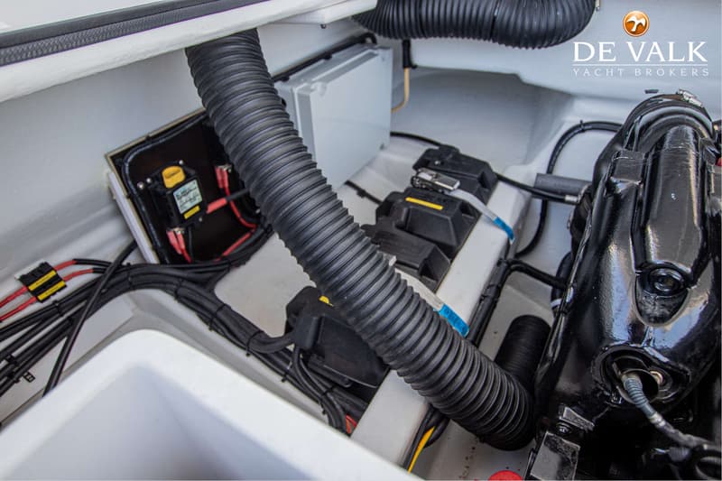 Een detailfoto van de motorruimte met een zwarte motor, kabels, slangen en een zekeringkast.