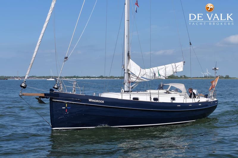 Een donkerblauwe zeilboot met de naam "Windroos" vaart op een zonnige dag over het water. — Bornrif 33