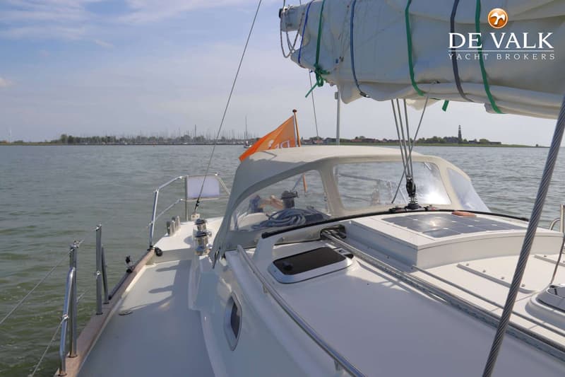 Een witte zeilboot met een opgerold zeil, een buiskap en zonnepanelen op het dek vaart op rustig water. — Bornrif 33