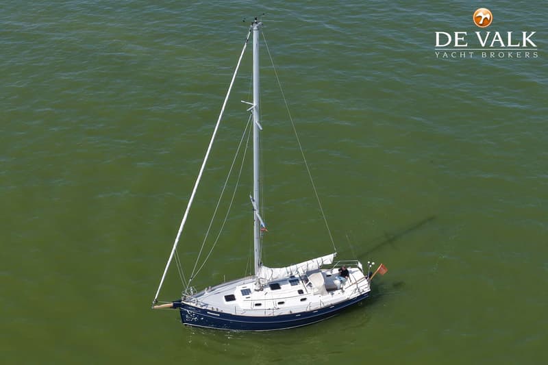 Een zeilboot met een donkerblauwe romp en witte opbouw ligt in groen water, met een persoon aan boord. — Bornrif 33