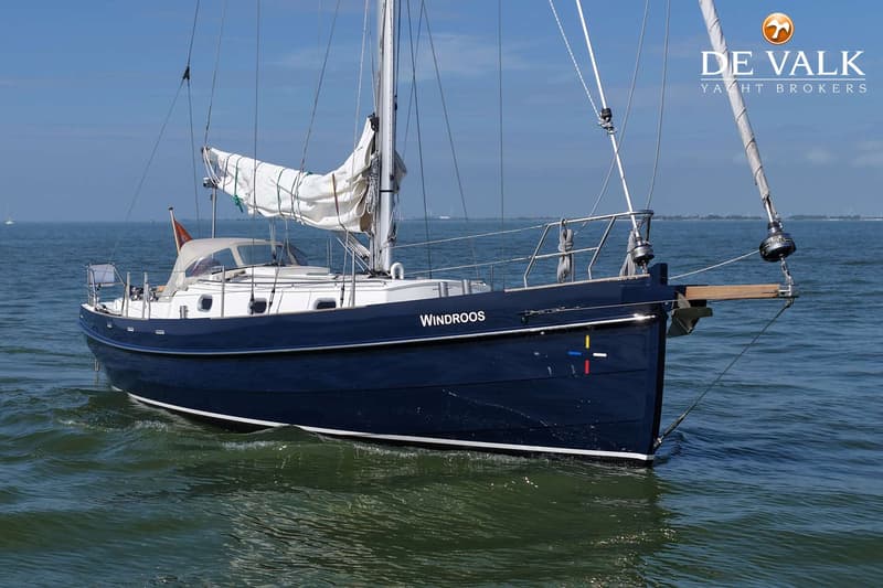 Een donkerblauwe zeilboot met de naam "Windroos" op de romp, drijft op het water onder een heldere hemel. — Bornrif 33