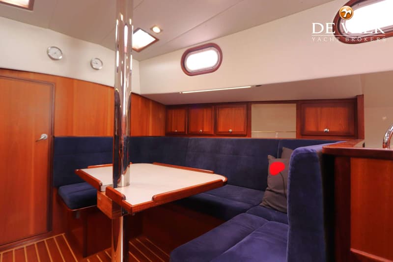 De foto toont een kajuit met een houten interieur, blauwe banken, een tafel en een patrijspoort. — Bornrif 33
