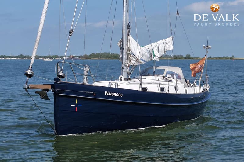 Een donkerblauwe zeilboot met de naam "Windroos" vaart op open water onder een heldere hemel. — Bornrif 33