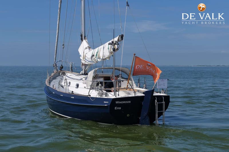 Een blauw-witte zeilboot met de naam "WINDROOS" en "Ens" op de spiegel, vaart op open water. — Bornrif 33